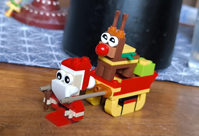 Ein Lego-Weihnachtsmann zieht einen Schlitten, auf dem Rentier Rudolph sitzt.