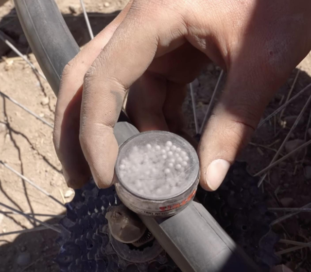 A hand holding a small container of styrofoam beads and running it across a bike inner tube, the beads start to “dance” when it is above the leak with air rushing out. 