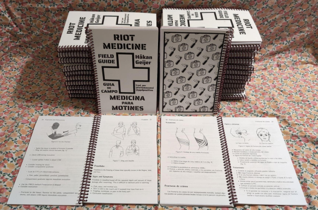a stack of books. front cover shows bilingual title with a medic cross. the back cover alternates molotovs with medic bags. open pages show texts and diagrams on how to care for various wounds and injuries.