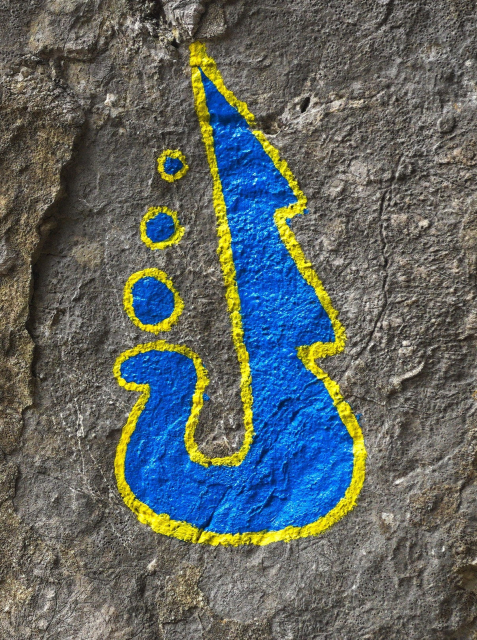 Zvláštní symbol na skále. Vypadá jako plachetnice. Modrý se žlutým ohraničením.