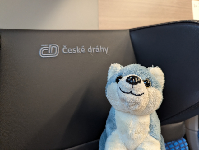 Small dog plushie next to Česke dráhy logo on a train seat