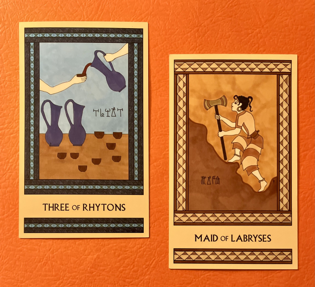 Two Minoan Tarot cards side by side on a bright orange background. Both cards have intricate, detailed borders. The Three of Rhytons, on the left, is painted in shades of blue and tan. It shows a table filled with two large pitchers and many small cups. Above the table, a hand holds a third pitcher, pouring wine into a cup held by another hand. The Maid of Labryses, on the right, is painted in shades of gold, cream, and tan. It shows a Minoan girl facing left, climbing up a rocky hillside as she holds a large labrys in both hands. 