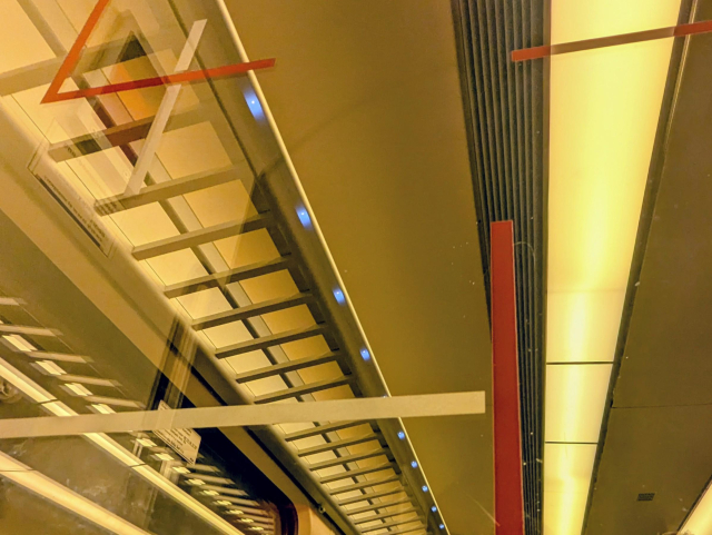 An indoor view from a SLT showing an overhead rack equipped with small LED lights as well as partition glass with red lines.