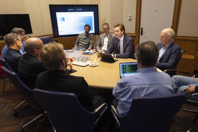 Room full of men round a meeting table. Bert viewed from behind with a prominent bald spot. On his screen green on black lettering. 