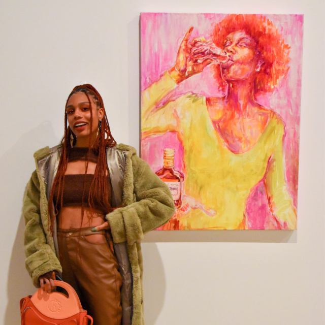 Jewel standing next to a painting of hers, she's a young Black woman