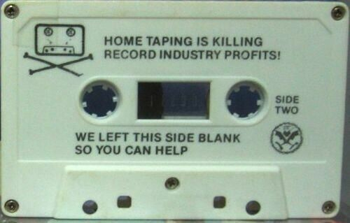 Photo of "Side Two" of an Alternative Tentacles cassette from the 80's. On the upper-right corner is an image of a cassette and crossbones, playing on the pirate skull & crossbones thing. The upper-middle contains text that reads "Home taping is killing record industry profits!" in all caps, underneath it says, "We left this side blank so you can help". To the right of the scond part, underneath the "side two" text, is the Alternative Tentacles logo, which depicts a cartoonish bat surrounded by a wreath of tentacles, holding a broken bomb in one claw, and a broken cross with a dollar sign on it in the other.