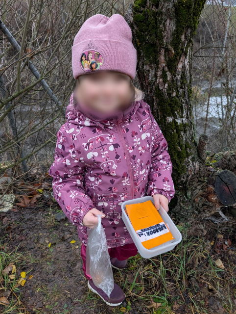 A girl in winter clothes holding a plastic box with a paper log. Her face is blurred.