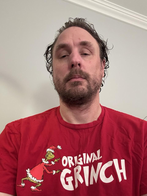 A picture of myself with bad hair wearing a red T-shirt that say “original grinch” with the grinch pushing the words to the right.