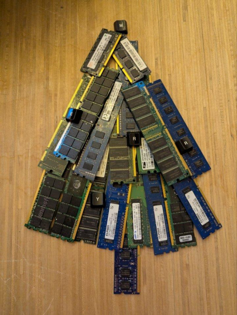 A Christmas tree made fromn computer memory chips. LOose keyboard keys are scattered across, spelling Merry