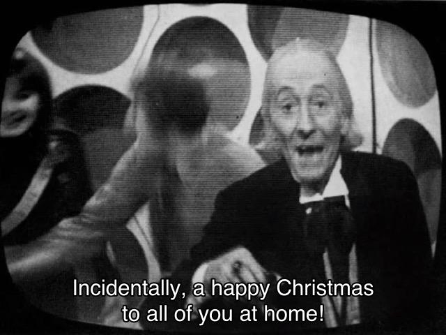 William Hartnell missing episode telesnap. The Doctor, Sara Kingdom and Steven Taylor are all standing around in the TARDIS having a toast. Steven is very blurry; Sara is barely visible. The Doctor is looking directly at the camera, and says, “Incidentally, a happy Christmas to all of you at home!”