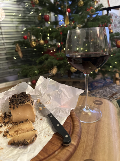 The cheese it is stinky. The red wine is robust and takes it in stride. A Christmas tree with dinky baubles stands in the background.