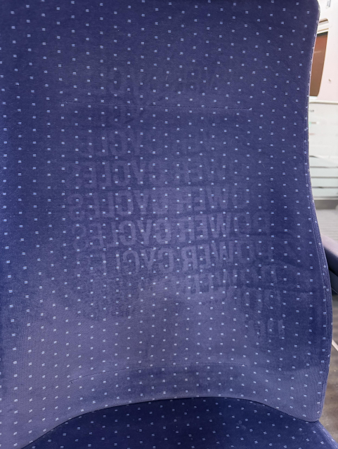 Foto der Rückenlehne eines DB-Zuges. In das Muster ist der mehrfache "POWER CYCLES"-Schriftzug von der Rückseite des 39C3-Merchs eingedrückt und als Muster zurückgeblieben.
