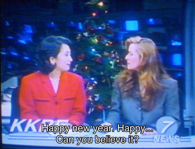 Paul McGann TV movie. (Another one, why not?) Two TV presenters are sitting in front of a Christmas tree on their set, looking at one another happily. Captions read, “Happy new year. Happy… Can you believe it?” “2000.”