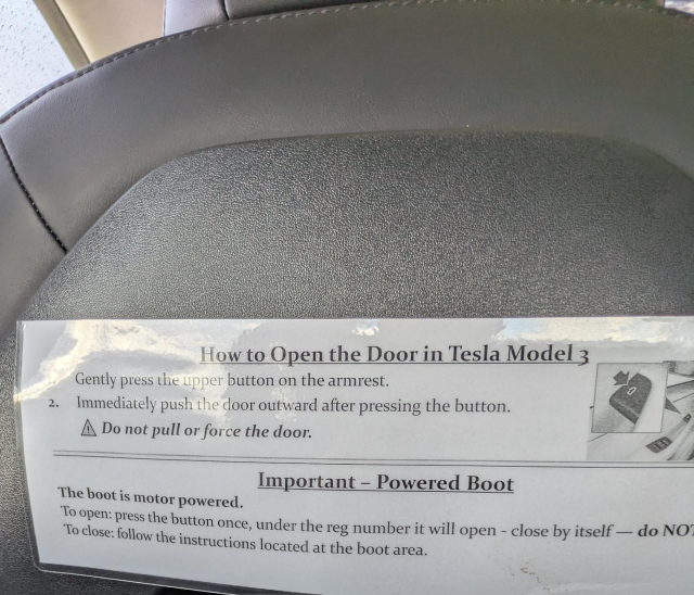 Sign in a showroom in front of a Tesla Model 3. Text reads:

How to Open the Door in Tesla Model 3

Gently press the upper button on the armrest.
Immediately push the door outward after pressing the button.
Do not pull or force the door.

Important - Powered Boot
The boot is motor powered.
To open: press the button once, under the reg number it will open - close by itself - do NOT (truncated)
To close: follow the instructions located at the boot area.