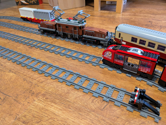 Picture of Lego Crocodile locomotive with passenger carriage from Bluebrixx, on the other track, there's Lego Downtown Tram. On the third track, there is a container car from Bluebrixx.