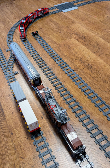 Picture of Lego Crocodile locomotive with passenger carriage from Bluebrixx, on the other track, there's Lego Downtown Tram. On the third track, Bluebrixx container car.