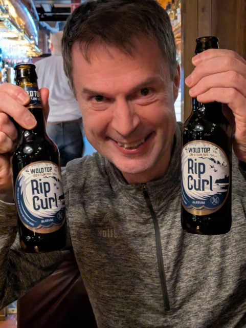 Daniel holding two beers labeled "rip curl" 