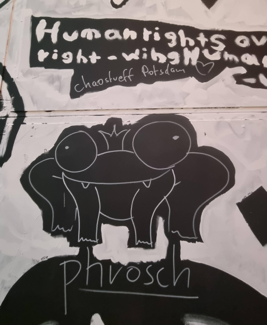 Weiß-auf-schwarz-Zeichnung auf einer Wand, u.a. ist ein Frosch gezeichnet mit "phrosch" drunter geschrieben. Darüber "Chaostreff Potsdam <3"