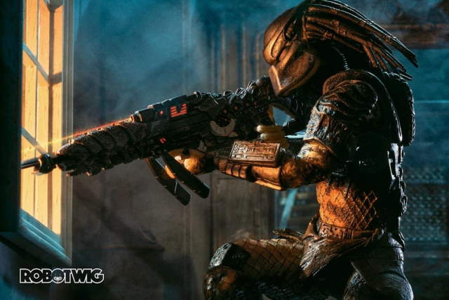 Predator aims its sniper weapon outside a window of an abandoned building. An orange glow comes from outside and shines through the window