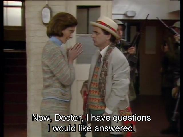 Sylvester McCoy episode. The Doctor is standing in a school hallway lined with armed soldiers, talking to Rachel Jensen, who’s looking at him quite cross. Captions read, “Now, Doctor, I have questions I would like answered.” The Doctor turns to leave, saying, “So have l. I’ll return in the morning.”