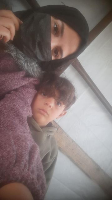 Baraa , a single woman wearing a medical mask, and her four-and-a-half-year-old son Ibrahim beside her, are looking directly at the camera.