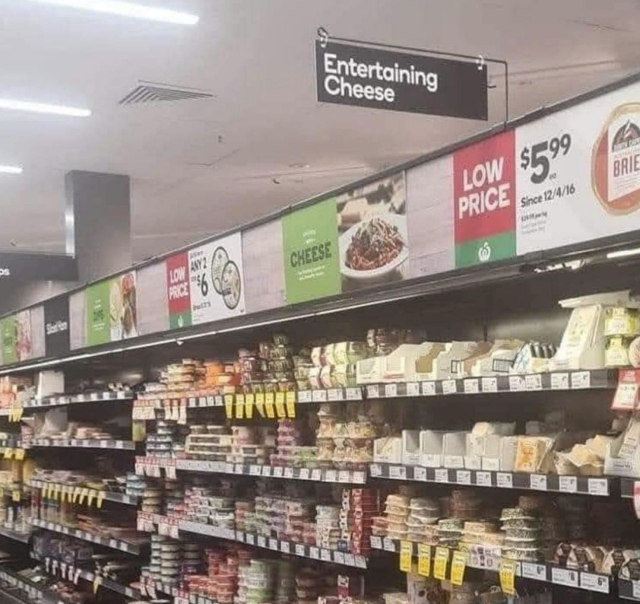 An aisle of cheeses and signs for cheeses with a sign saying "Entertaining Cheese"
