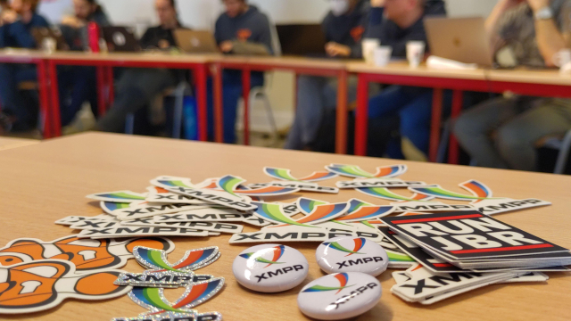 Various XMPP Stickers on a table and people at the summit blurred in the background.