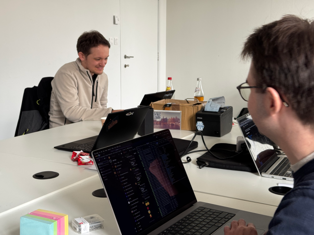 A picture of two people hacking on their laptops, next to a receipt printer.