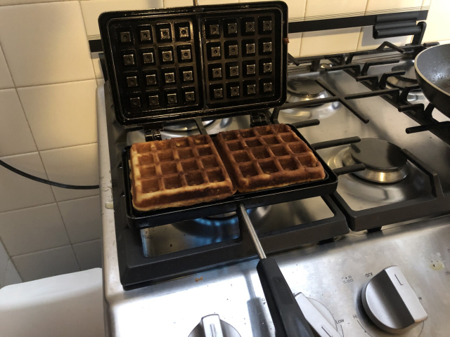 A waffle iron on the stove, with two waffles nice and brown.