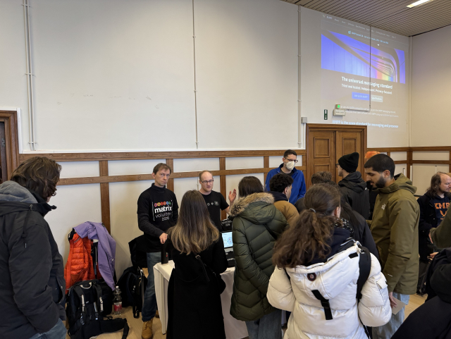 A photo of a crowded booth. The three people crew is talking to attendees.