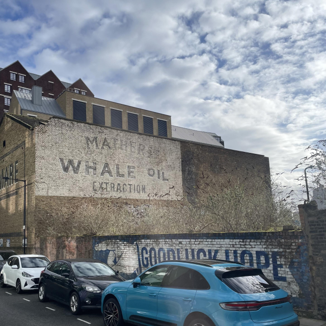 A large brick building with fading paint saying Mather’s Whale Oil Extraction. In the foreground a huge arm saying Goodluck Hope is painted on a brick wall.
