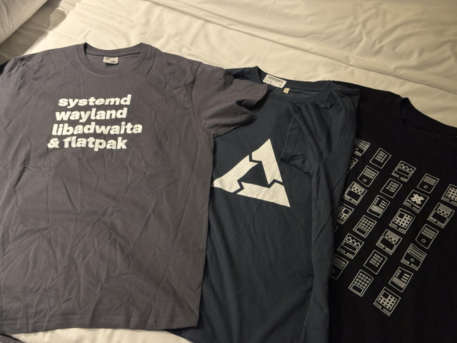 A picture of three T-shirts. One systemd/libadwaita, one postmarketOS and one Proxmox.