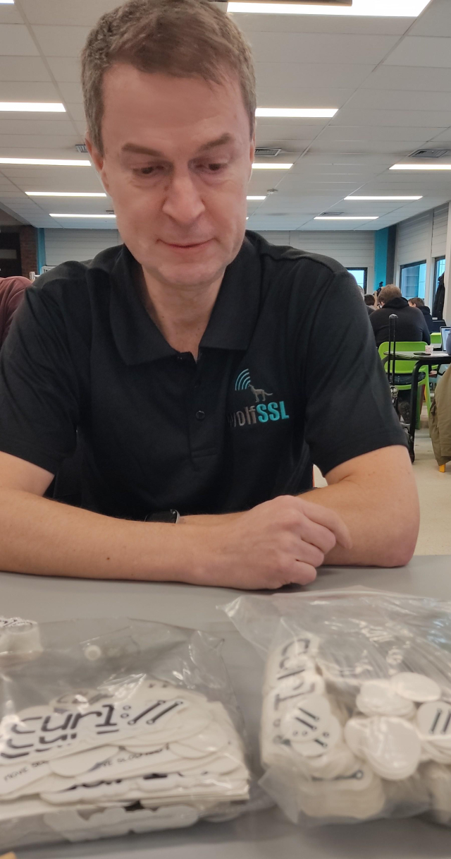 Daniel Stenberg sitting in front of a table with bags of stickers. The sad face is by accident but makes for a funny post