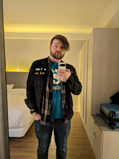 Cassidy wearing a GNOME shirt, black and gray flannel, and black denim jacket with a bunch of pins