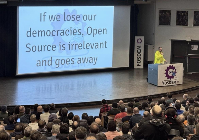 A full auditorium top level view of the stage and screen that says in large letters “If we lose our democracies, Open Source is irrelevant and goes away”