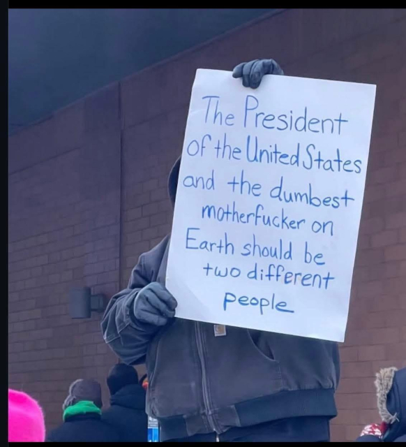 Photo of a man in winter clothes is standing outside holding a sign that reads, “The President of the United States and the dumbest motherfucker on earth should be two different people.”