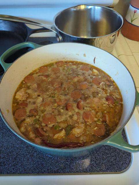 Red beans, sausage, salt pork, onion, celery, bell pepper, garlic, thyme, bay leaf, and black white and cayenne pepper simmering in a green enamelled Dutch oven