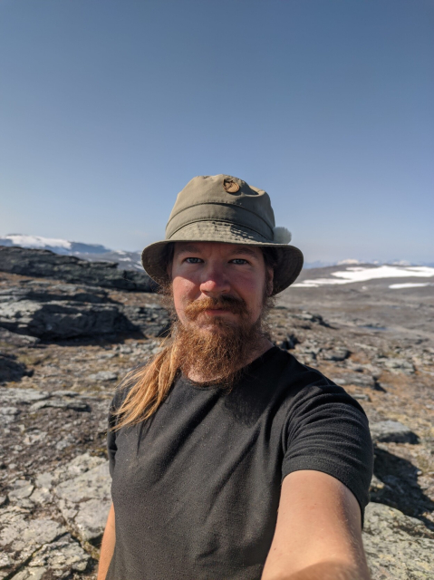 Me looking at the camera on a relatively barren mountaintop with some late-lying snow patches.